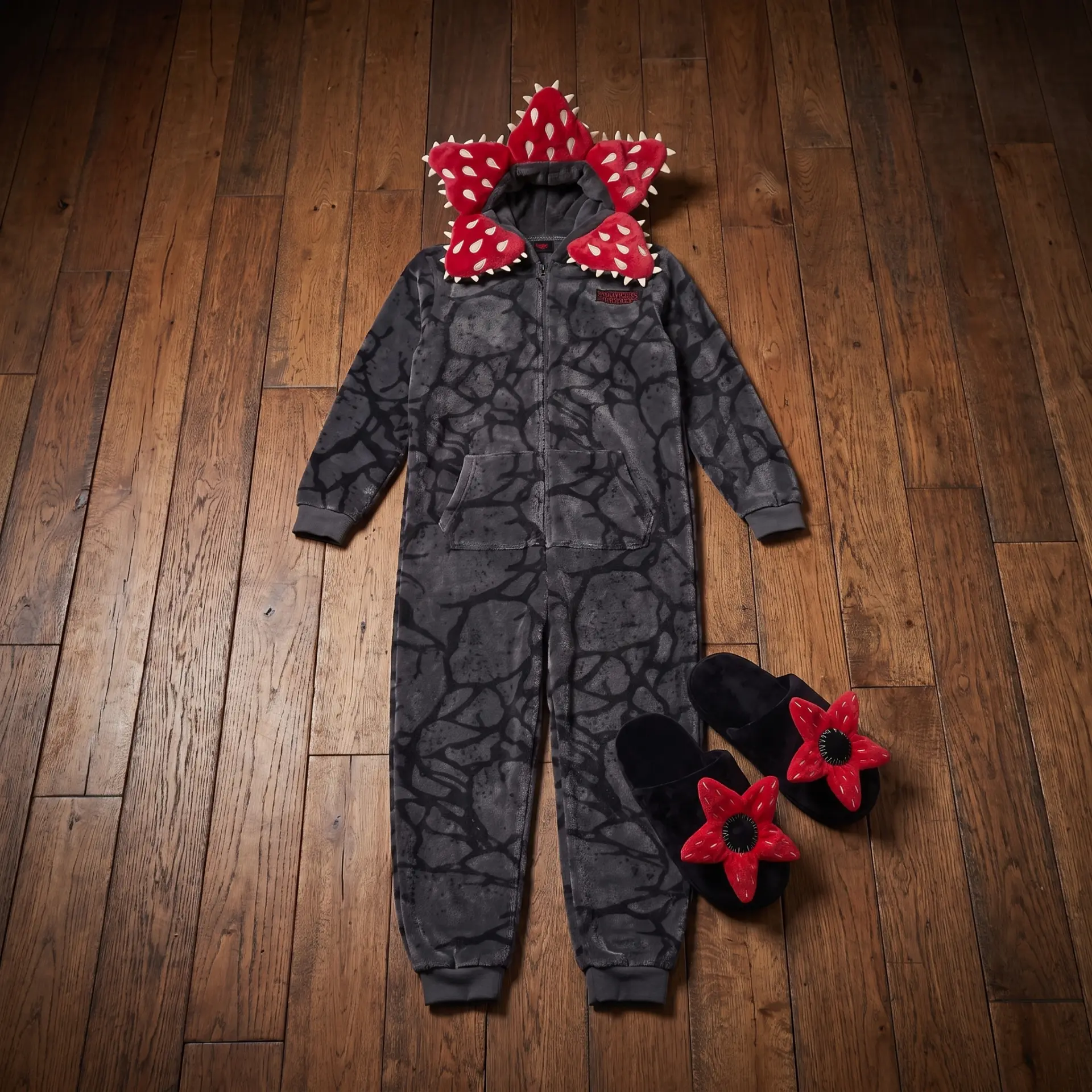 Grey fleece hooded onesie with red spiked crown laid flat beside matching black slippers